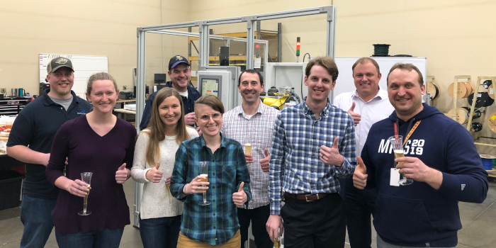 A group of people, possibly employees and customers, standing together in an industrial setting, smiling and posing for the camera.