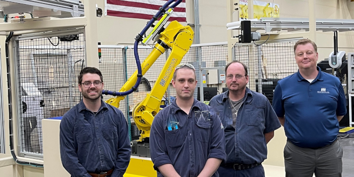 Another group of people gathered in front of a robotic automation setup, some holding glasses, indicating a celebratory event.