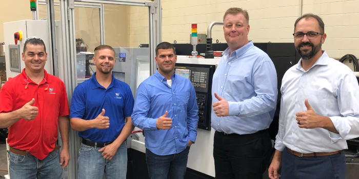 People in an industrial environment, standing together, smiling, and posing for a group photo.